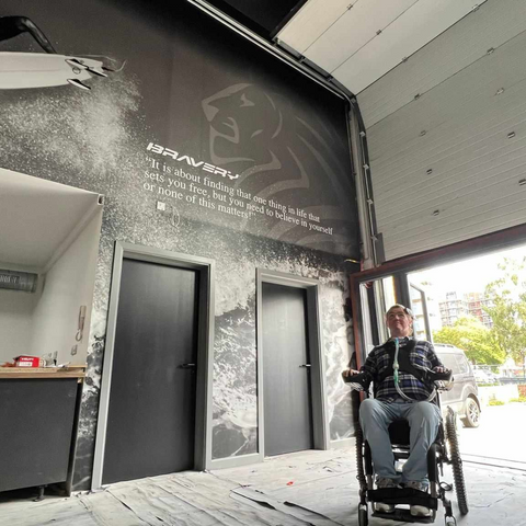 Toby in his wheelchair sat inside the Bravery building next to one of the vinyl wrapped walls.