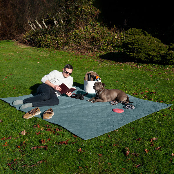 A human and dog hanging out in the sun on the grass, lying on top of a FurHaven Quilted Twill Waterproof Bed/Furniture Protector