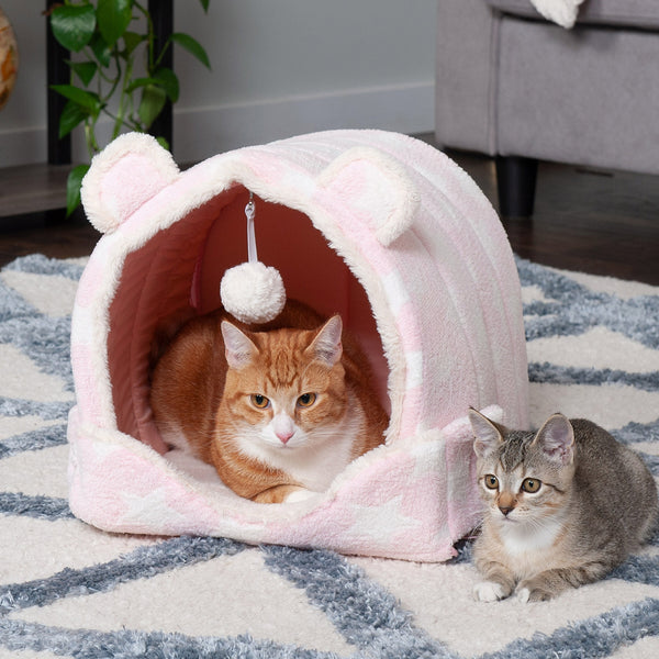 An orange cat and a gray kitten sitting both inside and next to a FurHaven Fleece Cozy Cave Bed.
