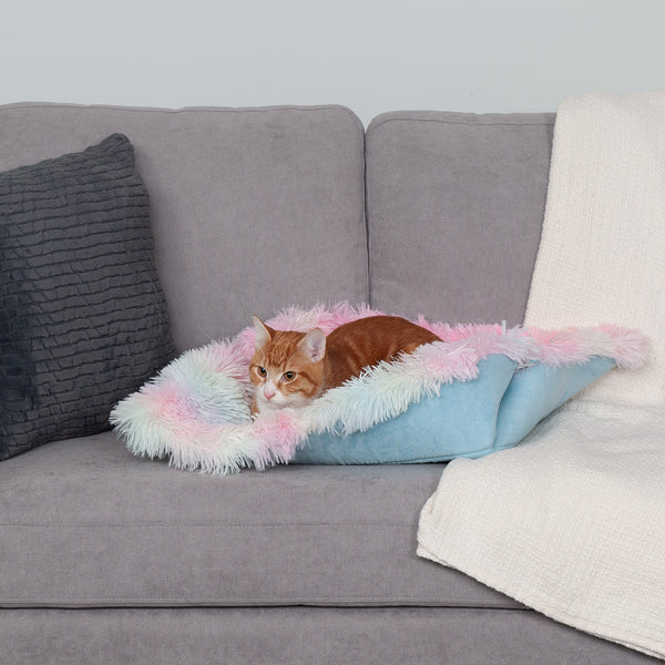 An orange and white cat lying in a FurHaven Self-Warming Convertible Cuddle Pet Mat & Bed, both of which are on a gray couch