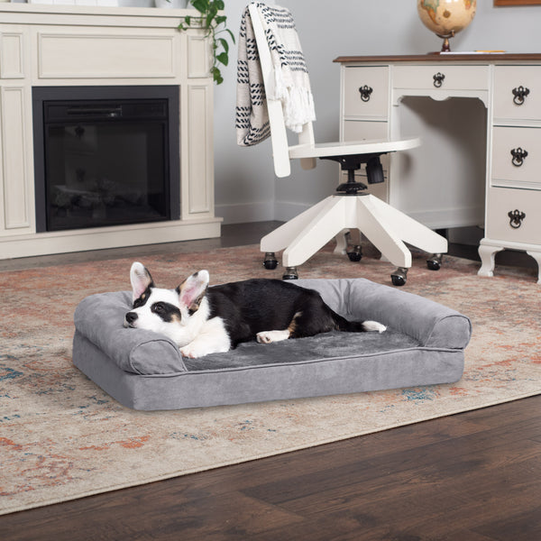 A black, brown, and white dog lying on a FurHaven Sofa Dog Bed, both of which are on a carpet on top of hardwood floor, in front of a fireplace