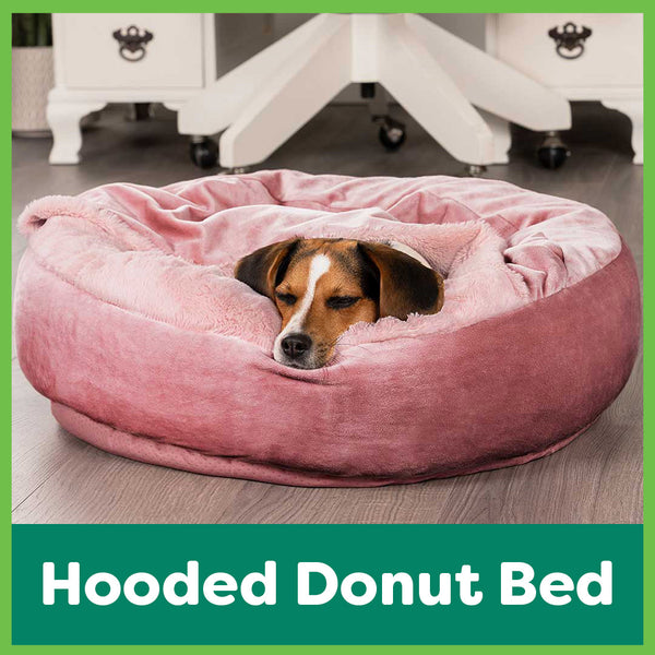 A white, black, and tan beagle is asleep in a pink donut dog bed with a built in blanket top at FurHaven Pet Products.