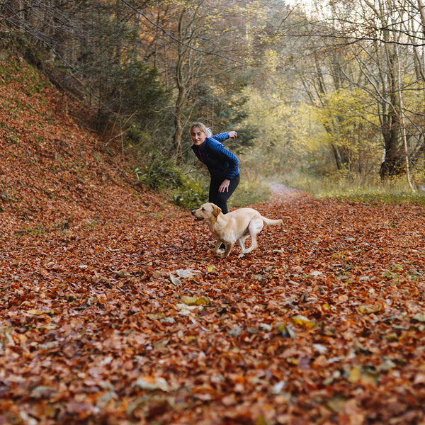 A human in a blue jacket about to throw a ball for their golden retriever dog in a leaf strewn knoll at FurHaven Pet Products