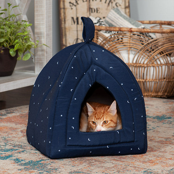 An orange and white cat lies within a FurHaven Insulated Pet Bed Tent on a rug on the floor