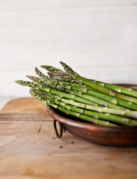 Long and green asparagus stalks in a brown bowl on a wooden table at Furhaven Pet Products