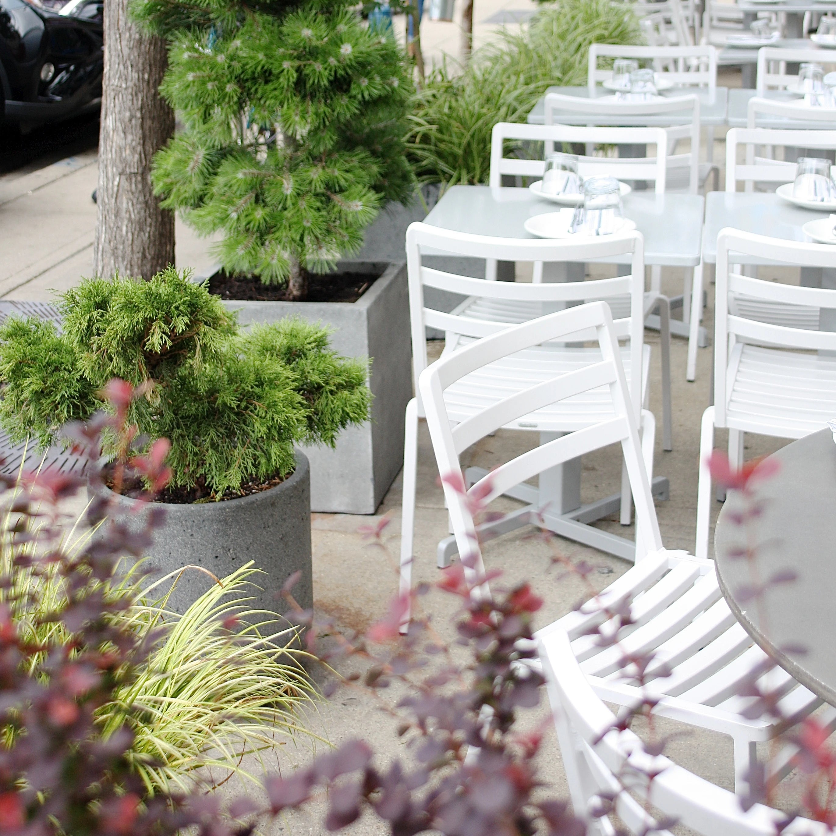 Outdoor patio with planted containers and white tables and chairs