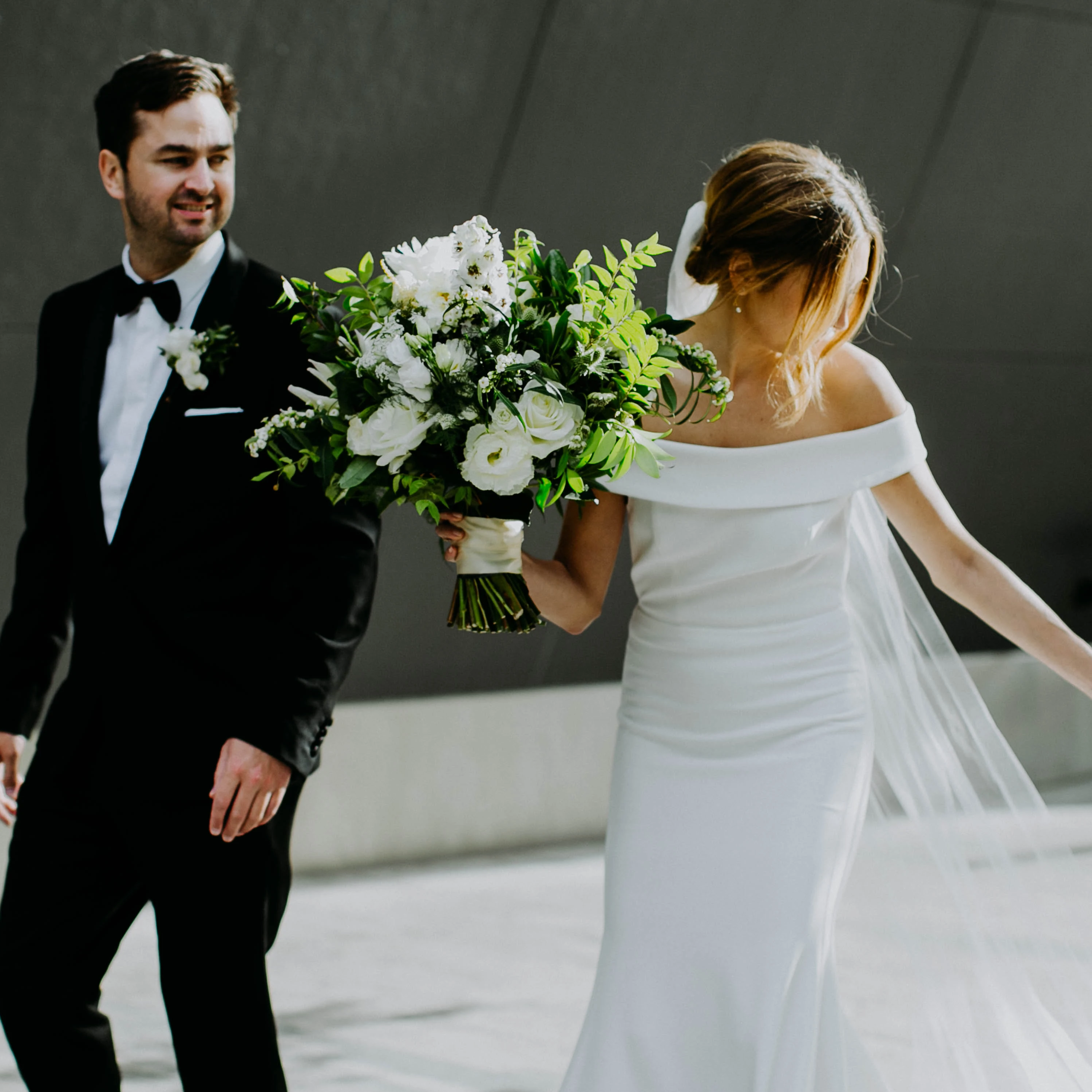Bride and groom walking in the city, bride holds a large white and green bouquet