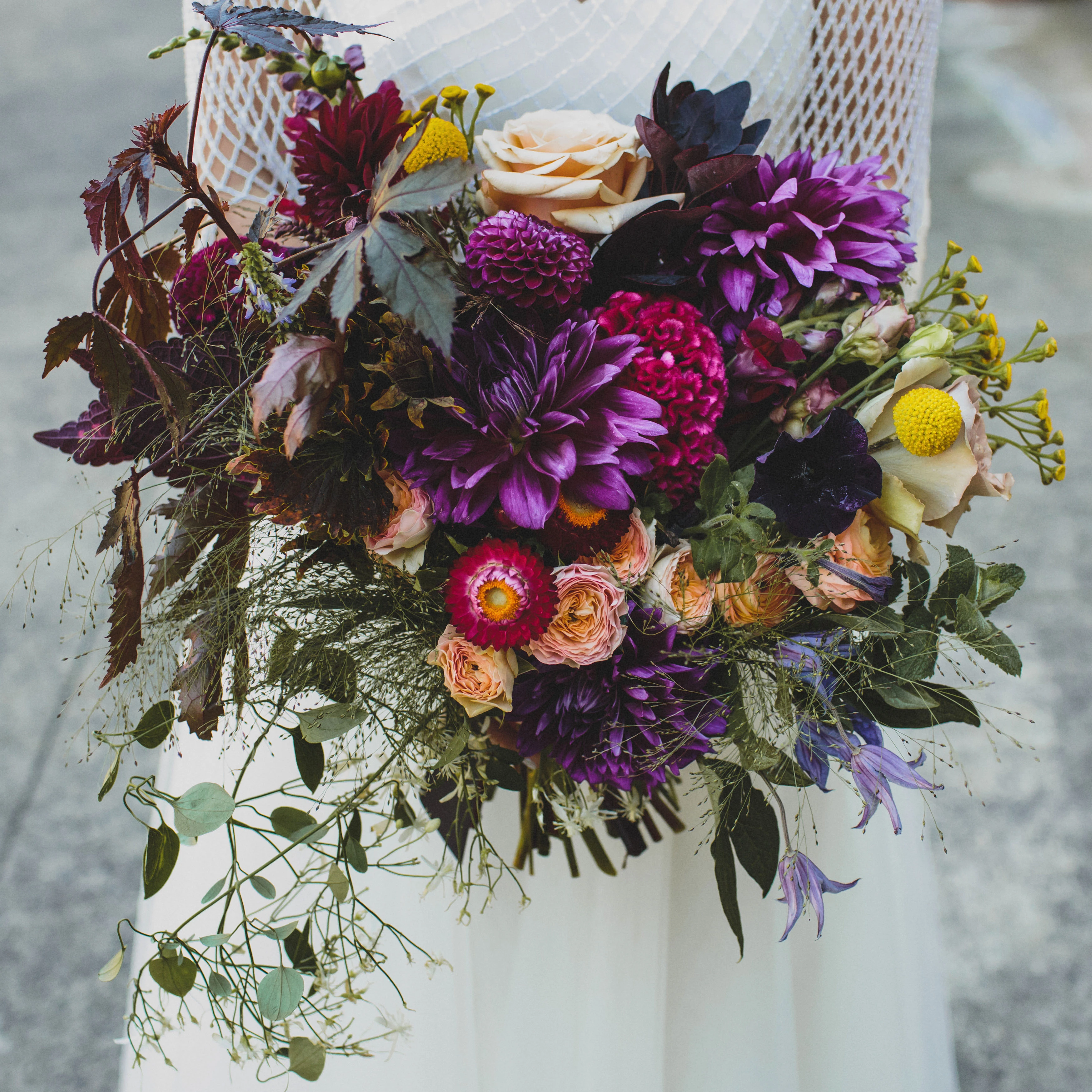 Person in white dress holding vibrant purple and orange bouquet with deep green foliage