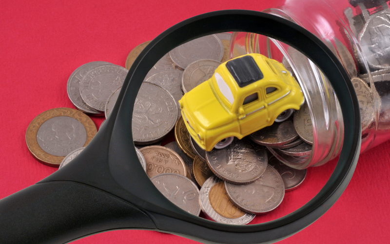 yellow toy car and several coins in a jar under a magnifying glass