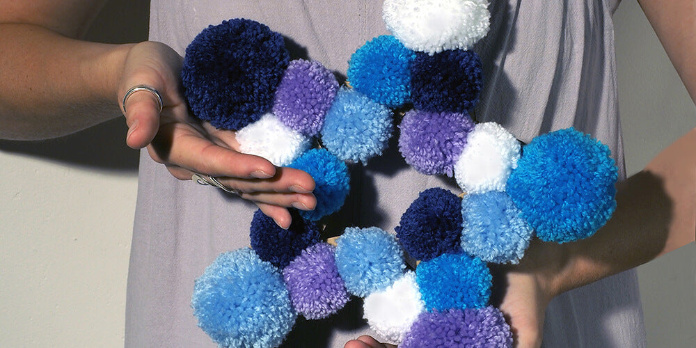 Emma holding pom pom star wreath in her hands with dungarees in background.