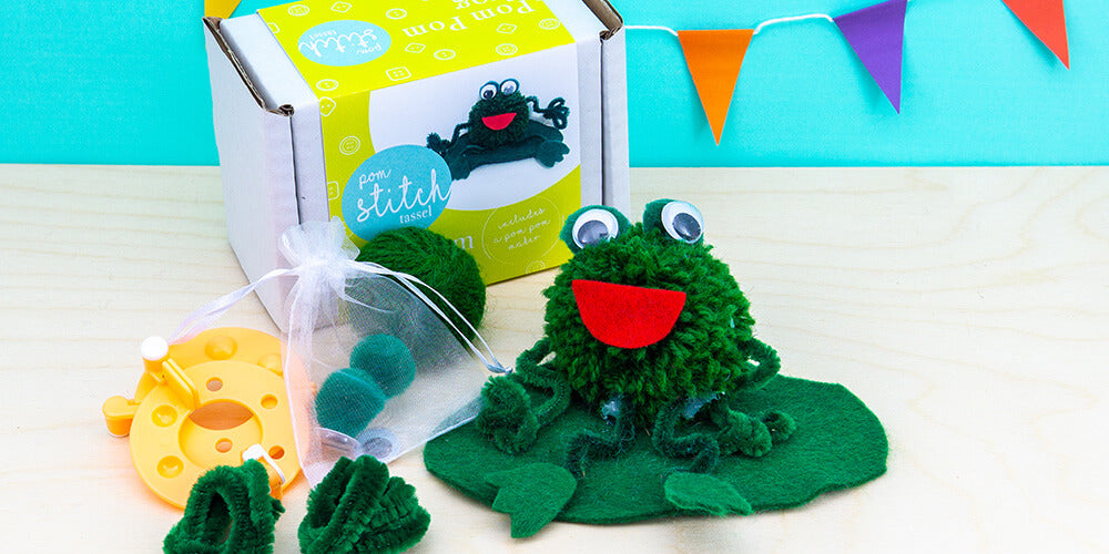Pom pom frog craft kit - make your own pom pom animals - a photo of the pom pom frog, craft kit and all the materials included with blue background.