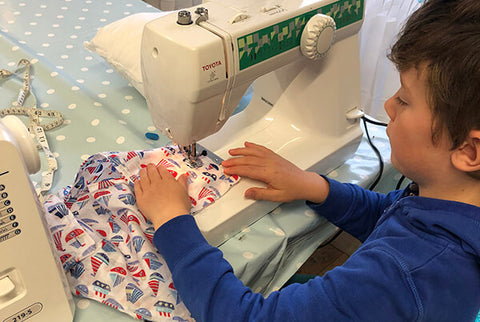 Stitch club - a little boy sewing nautical fabric on a sewing machine with polka dot table cloth.