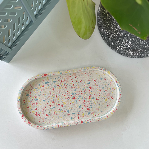 The terrazzo collection trinket tray in rainbow colours on white desk with house plant.
