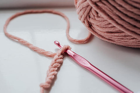 crochet club - ball of pink wool and crochet hook on white table