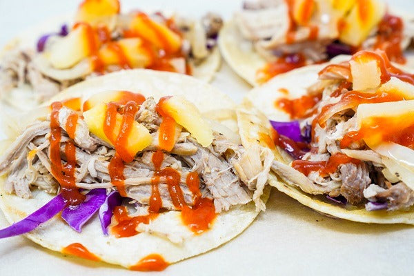 A close up shot of shredded pork tacos with pineapple at hot sauce.