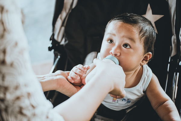 Asian toddler looking trustingly at mother while drinking from milk bottle.