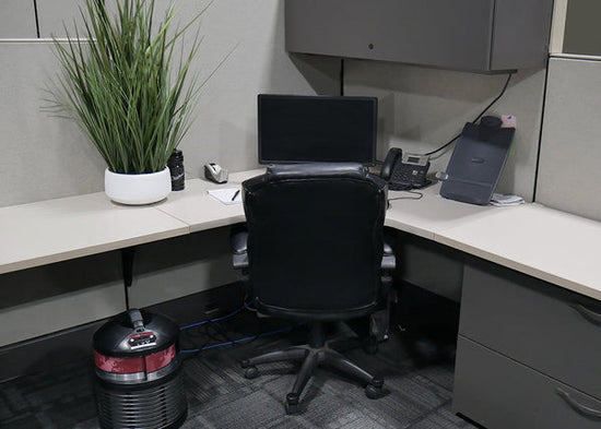 Cubicle air purifier on floor next to desk.