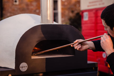 Barney placing a pizza into a wood fired pizza oven 