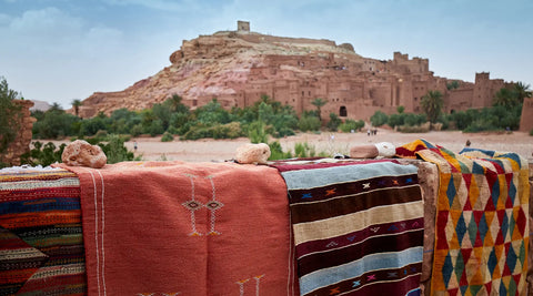 A picture showing Handmade Moroccan rugs in front of Aït Benhaddou a historic castle in Morocco.