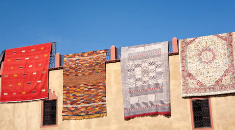 Handmade Moroccan rugs hung on a metal railing and earthen wall.