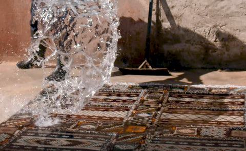 photo showing a man spilling water on a handmade moroccan rug for traditional cleaning
