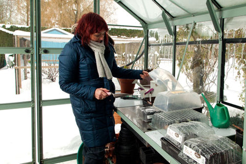 Red-haired woman inside a Rhino Greenhouse with snow outside. She is checking on her seedlings inside a propagator