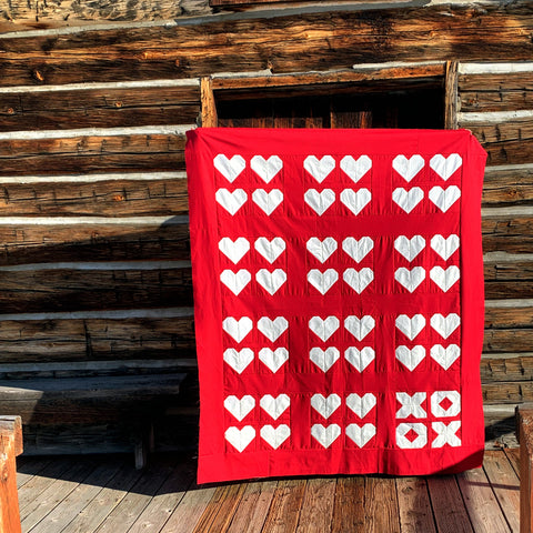 Red and white heart quilt in front of log building