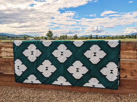 Green and white modern quilt on fence with clouds in the sky.