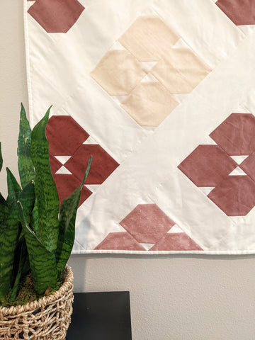 Simple modern quilt top in shades of pink and white with green plant in front on table.