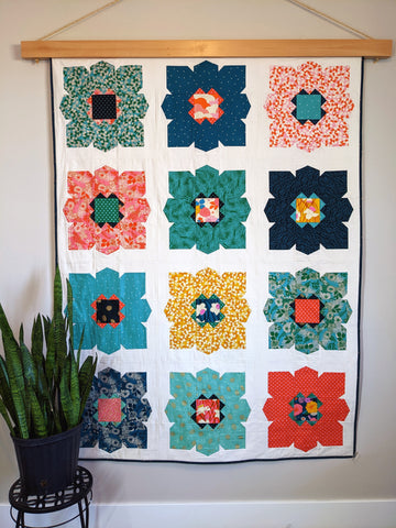 Large flower quilt with blues, greens, orange, pink and yellow flowers and white background,