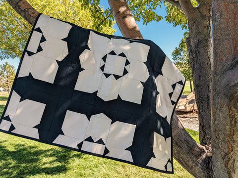 Large flower black and tan quilt hanging in tree.