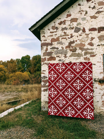 Red and white snowflake quilt in front of old stone building
