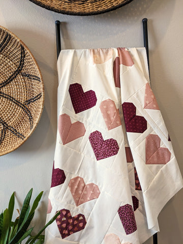 Pink heart quilt with white background on ladder with basket and plant