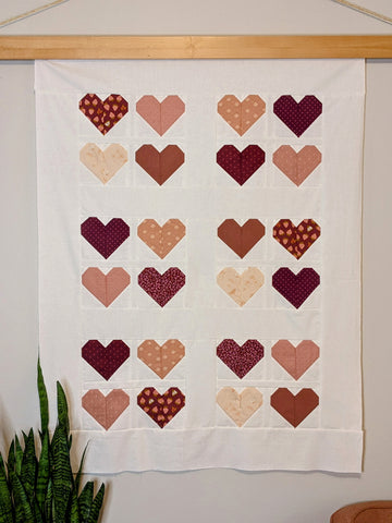 Pink and white heart quilt on wall with plant