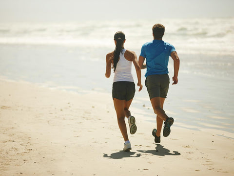 A man and woman running on the beach, staying fit on the road
