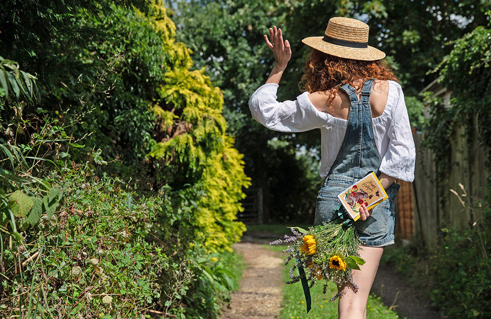 girl walking down country lane with greeting card and flowers