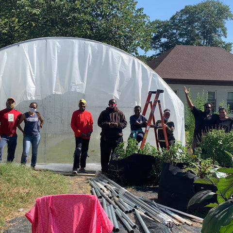 Sunny day photo of 8 volunteers standing in front of plastic-covered hoop house on the farm.