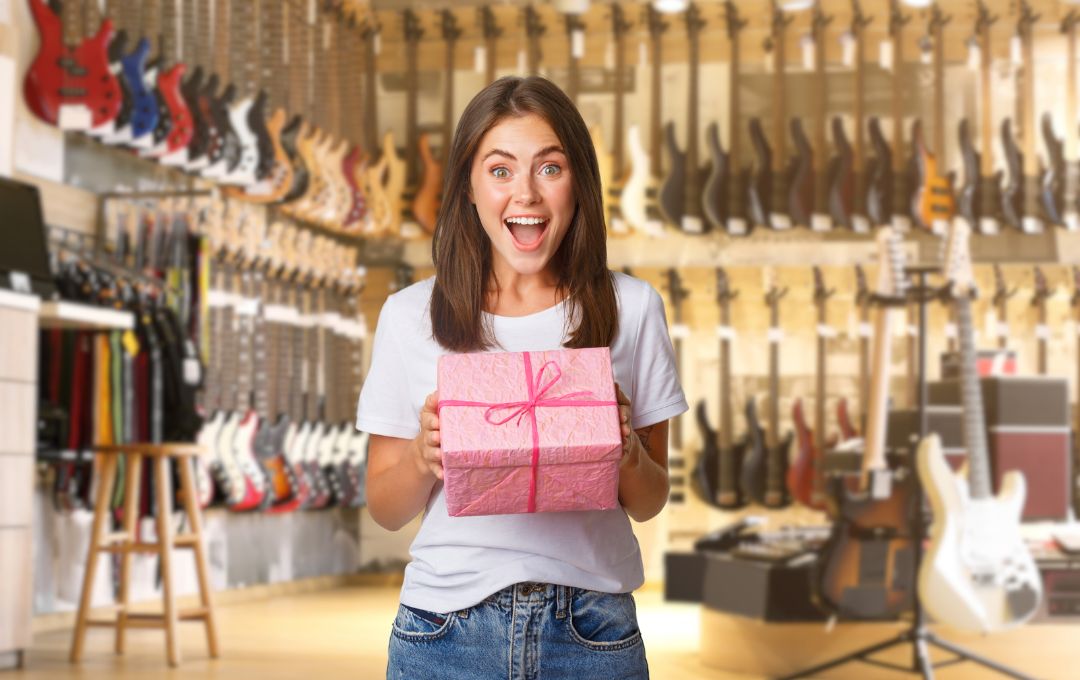 a happy woman holding a gift box inside of a guitar store