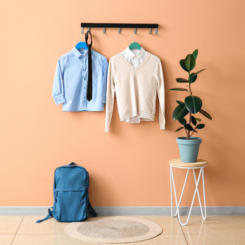 Two children's school uniforms hanging by an orange wall