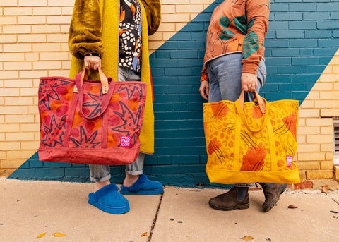two women holding a yellow and maroon tote bag with colorful designs