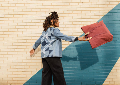 girl walking down sidewalk swinging a big maroon colored bag in front of a yellow and blue wall