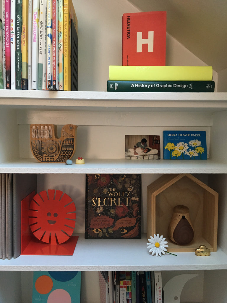 Straight on photo of a built-in bookshelf in Meenal's studio that is filled with children's books, art and design history books, art books, paper swatchbooks, old photos, and old cherished items.
