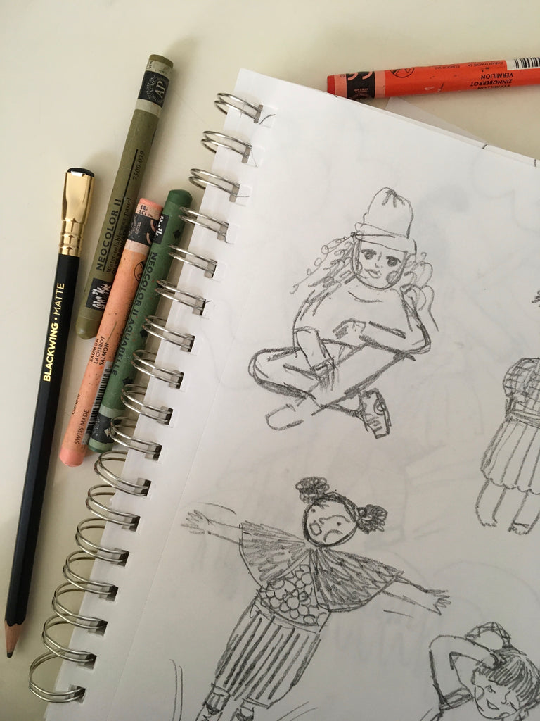 Photo of part of a spiral bound sketchbook with smudgy pencil sketches of kids. Pencil and crayons scattered around sketchbook.