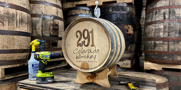 A 10 Gallon Distillery 291 Colorado Whiskey Barrel with a Vinnie nail and tools for installing the nail – a hammer, drill and sanitizing spray bottle.