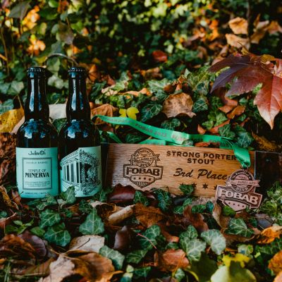 Two bottles of Double Barrel Temple of Minerva and a barrel stave FOBAB award in front of a leafy background