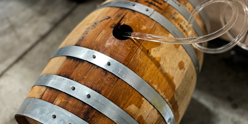 An oak barrel being filled through the bunghole with a small hose