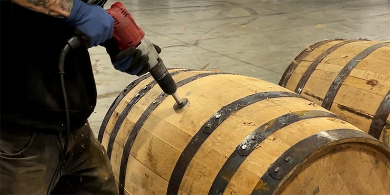 Midwest Barrel Co team member drilling belly bung hole in a head bung whiskey barrel while barrels sit on racks