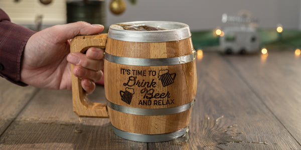 Hand holding wood barrel mug engraved with text It's time to drink beer and relax next to two beer mug drawings