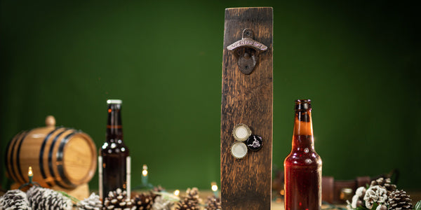 Whiskey barrel stave bottle opener with beer bottles, pine cones and oak aging barrel in background