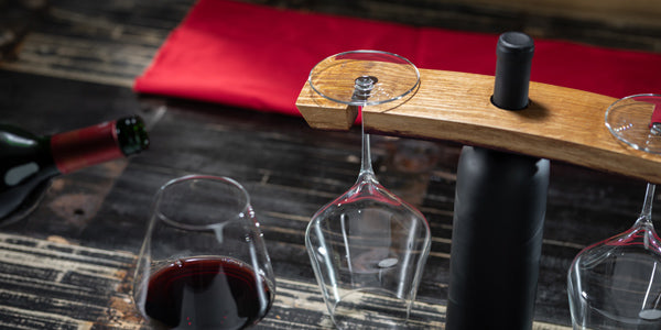 A glass of red wine being poured with a wine barrel stave caddy holding a bottle and two empty wine glasses